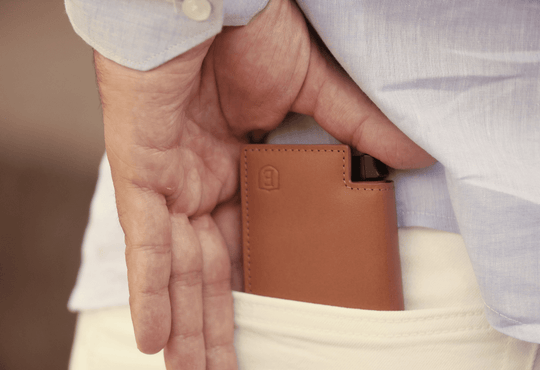 man putting slim brown leather wallet in his back pocket