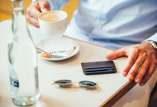 a cardholder wallet on a table next to a cup of coffee and sunglasses